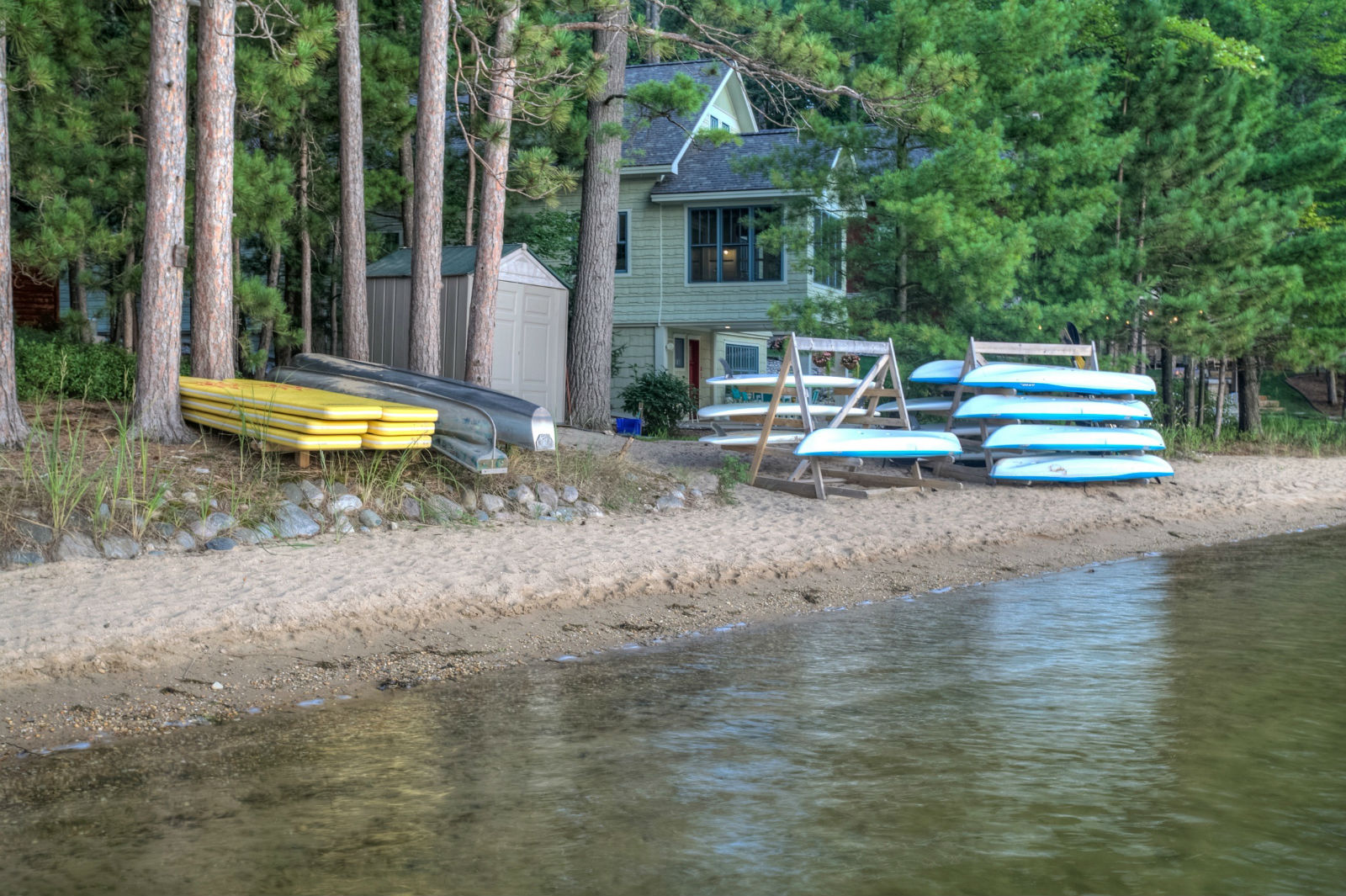 Stand-up paddleboards and kayaks lined up on Lakemore's private sandy beach on Arbutus Lake